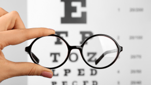 a pair of round glasses held up in front of an eye exam chart