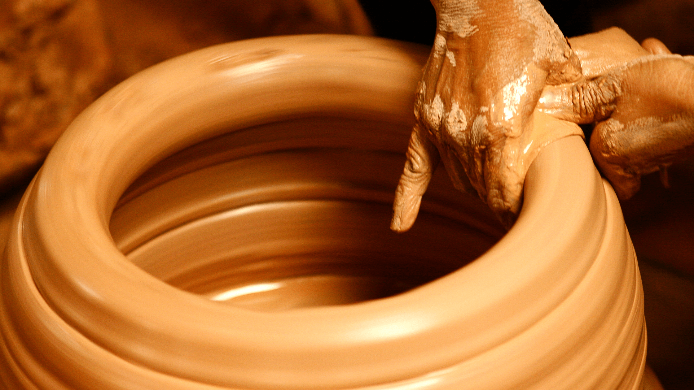 a potter's hands shaping a lump of clay into a pot