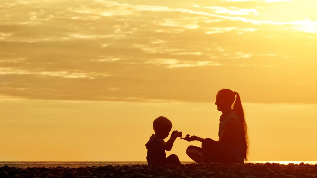 silhouette of mother with her child calmly playing on a beach at sunset
