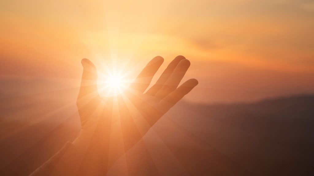 a hand raised to look like the sun is rising from it with a mountain silhouette in the background