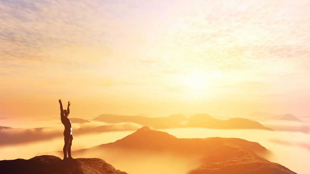 silhoutte of a person at the top of a mountain at sunset