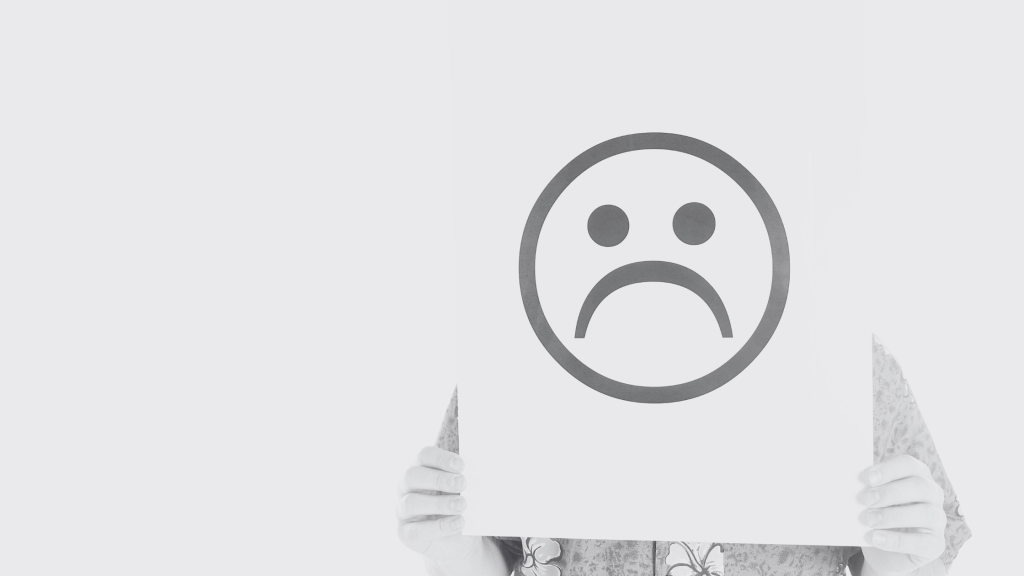 person holding up a frowning face sign in front of their own face