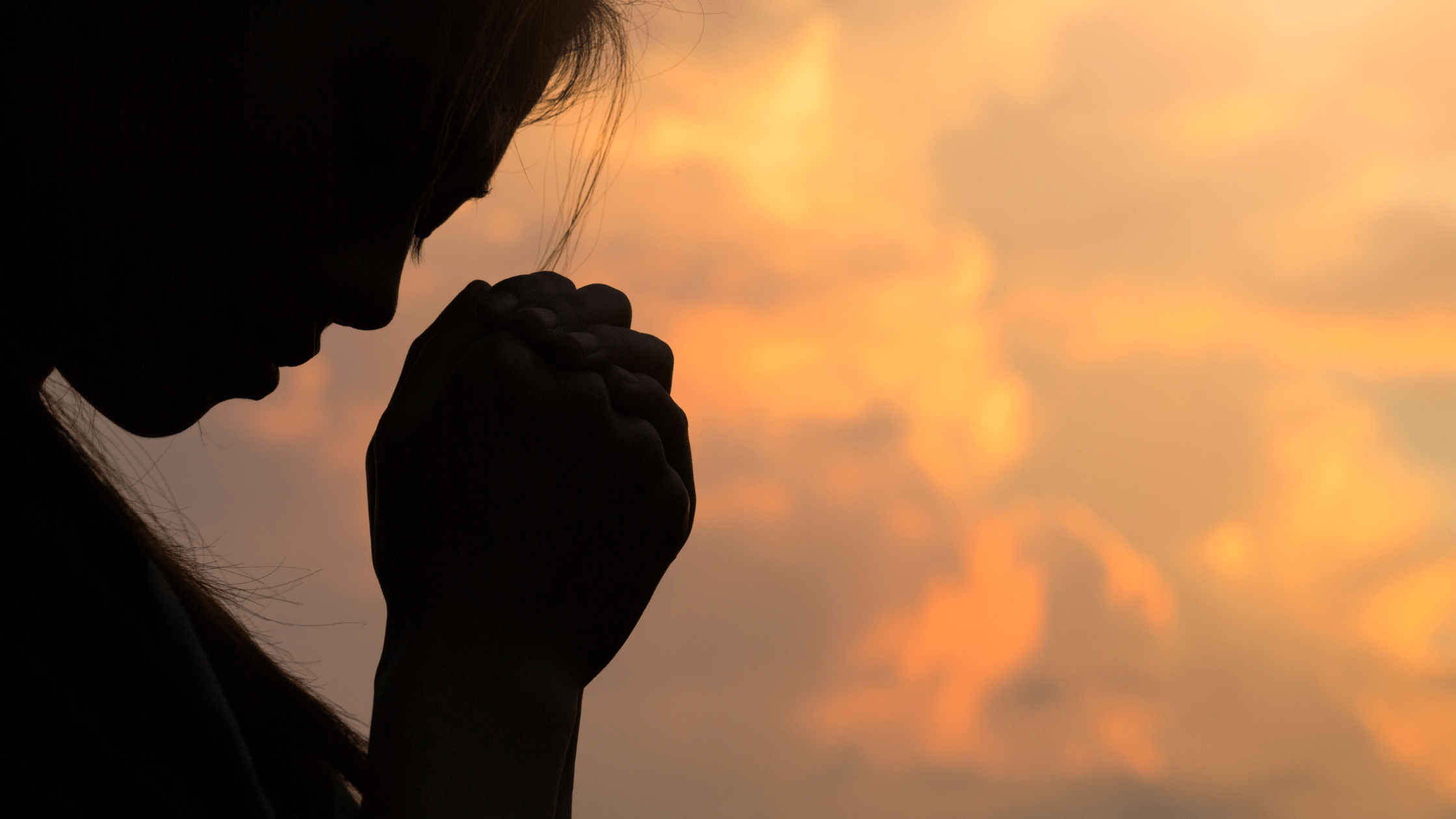 silhouette of a woman with her hands folded and her head bowed in prayer