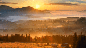 glorious mountain range at sunrise with glowing forest and fields in the foreground