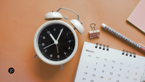 An alarm clock beside a calendar, paper, and pencil to signify patient trust in God's timing for your writing