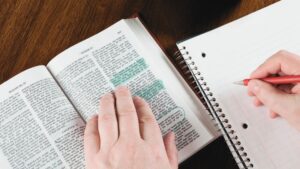 A woman writing in a notebook while studying the Bible that contains highlighted verses
