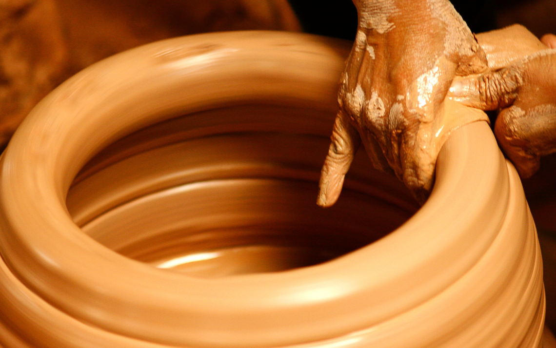 a potter's hands shaping a lump of clay into a pot