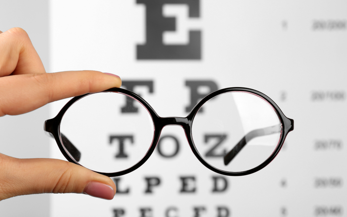 a pair of round glasses held up in front of an eye exam chart