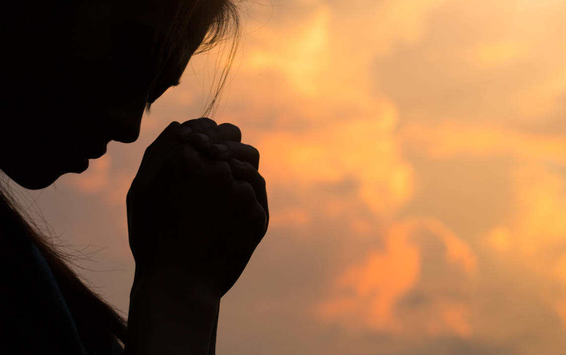 silhouette of a woman with her hands folded and her head bowed in prayer